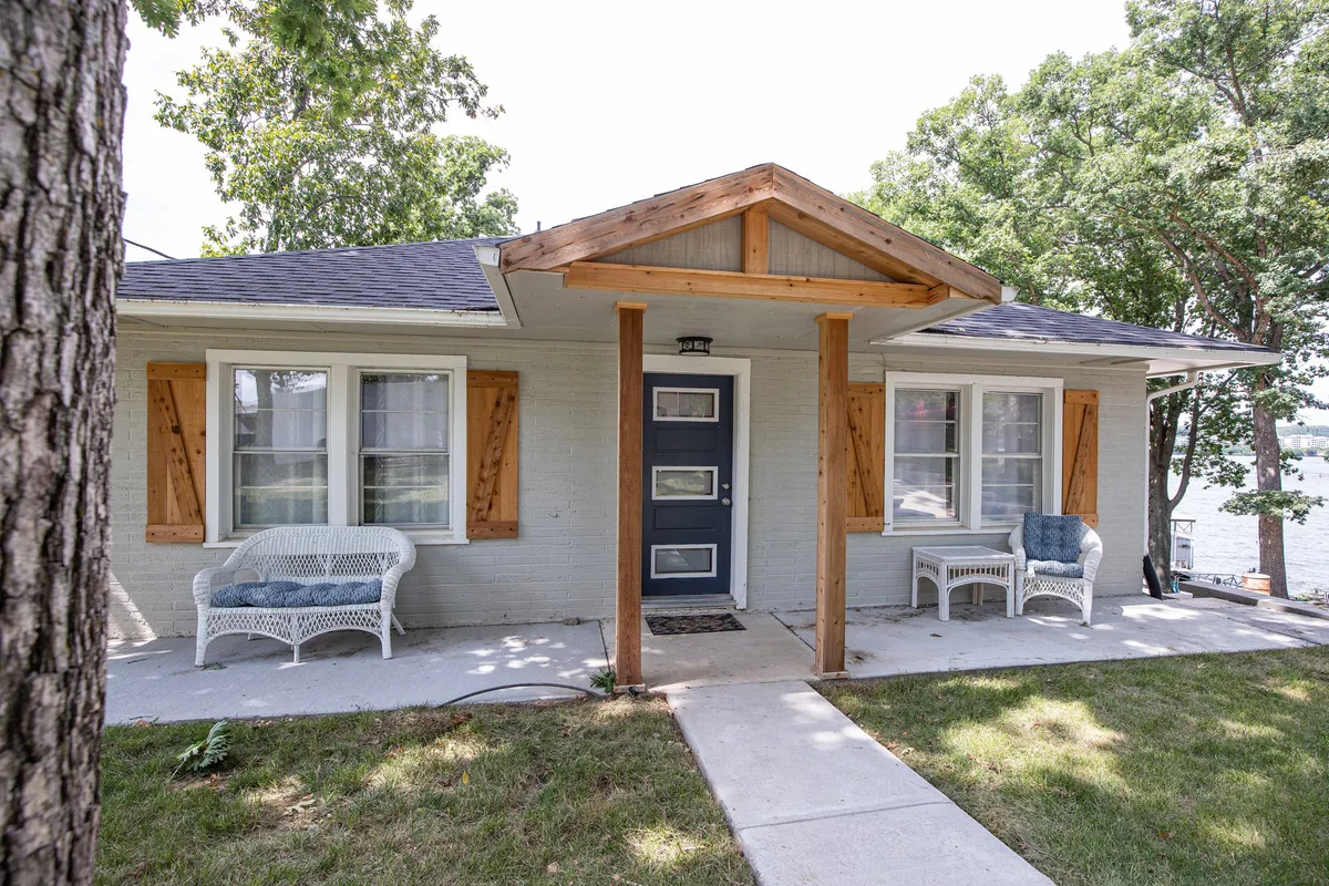 A welcoming front porch featuring wicker furniture, lush landscaping, and a view that hints at the lakeside setting. The space feels open and inviting, suggesting a peaceful connection between the home and outdoors—ideal for socializing or winding down after a day of exploration.