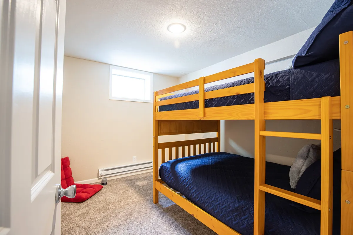 A playful and cozy kids' bedroom with a bunk bed, red bean bag chair, and a window letting in daylight. The space suggests fun sleepovers or quiet moments, designed for younger guests or families.