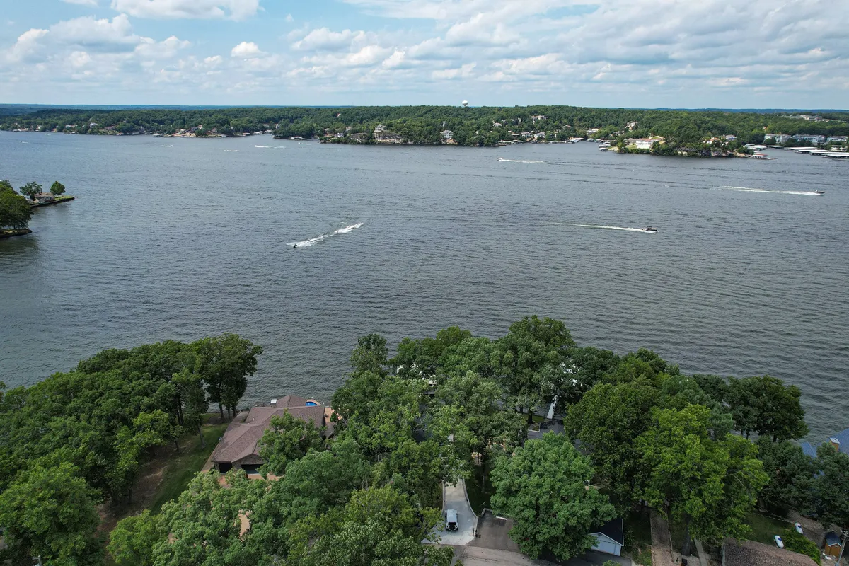 A wide view of the expansive lake, surrounded by greenery and dotted with boats, sets a serene lakeside atmosphere. The image conveys natural beauty and the area's appeal for boating or waterfront dining.